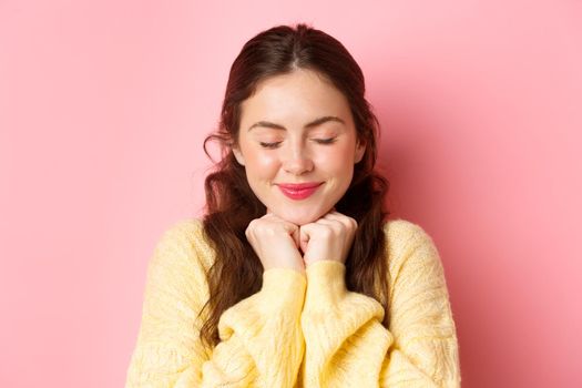 Close up of lovely brunette woman daydreaming, close eyes and smiling, thinking of romantic moment, standing happy against pink background in tender pose.