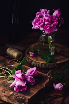 Pink garden roses on wooden table and in jar with water