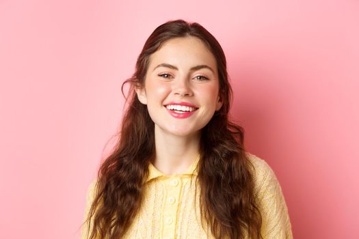 Close up of happy carefree lady laughing and smiling, looking pleased and relaxed at camera, standing against pink background.