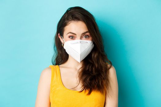 Covid-19, coronavirus and social distancing. Attractive young woman wearing respirator from coronavirus, looking at camera, blue background.