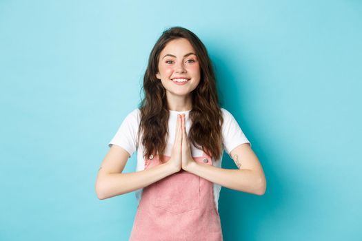 Thank you. Smiling cute girl showing namaste, gratitude gesture, asking for help or favour, smiling pleased, thanking for favour, standing over blue background.