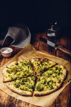 Sliced Italian pizza with broccoli, pesto sauce, spices and cheese on baking paper