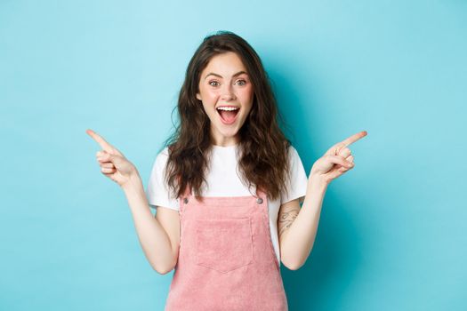 Pick your side. Smiling excited woman screaming of joy, pointing fingers sideways at left and right copy space, showing advertisement good deal, standing against blue background.