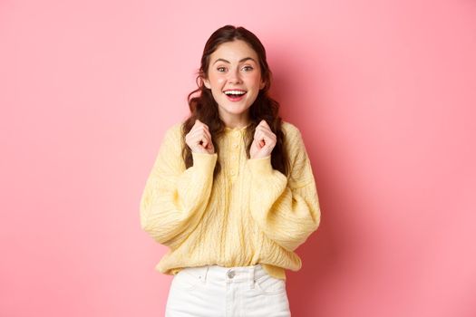 Image of hopeful lucky girl looking at camera, wants to win, waiting for important results, standing against pink background.