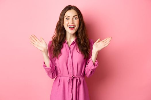 Cheerful attractive lady scream of joy and clap hands, looking at camera, hear great news, rejoicing, standing over pink background.