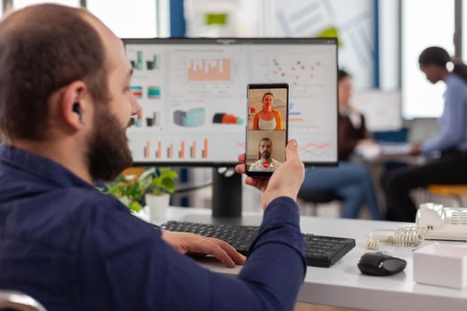 Handicapped invalid manager talking on videocall with friends holding smartphone taking break during work time. Employee sitting immobilized in wheelchair working in financial business office.