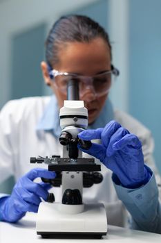 Biologist doctor using medical microscope analyzing blood sample working at microbiology experiment in hospital laboratory. Chemist researcher developing vaccine against virus disease