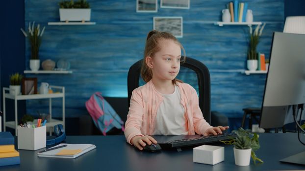 Elementary school child using computer and keyboard at desk for homework and learning. Little girl looking at monitor for online remote class lessons on internet connection at home.