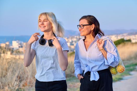 Beautiful talking mom and teenage daughter outdoors. Happy mother and teen girl walking together with eco shopper with oranges. Family, happiness, relationship parent teenager, summer, trendy, people