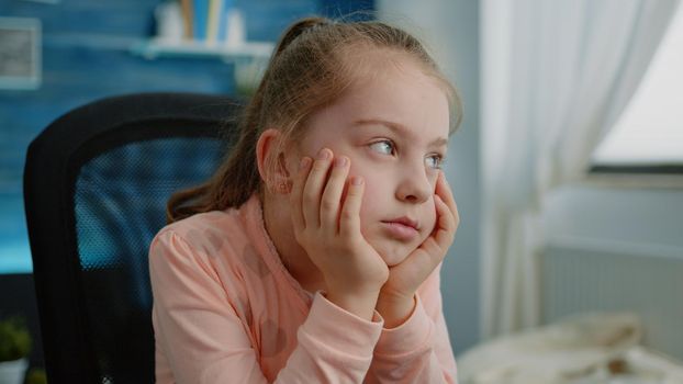 Close up of tired child listening to remote online lesson for school work at home. Exhausted young girl looking at screen for learning and class tasks while sitting at desk, falling asleep