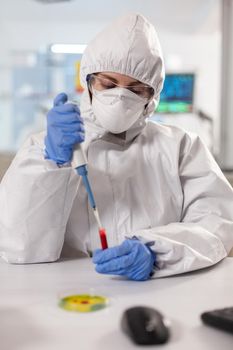 Scientist dressed in ppe suit taking blood sample using micropipette. Scientist dressed in ppe suit taking blood sample Chemist in coverall working with various bacteria, tissue blood samples for antibiotics research.