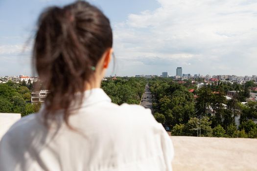 Back front of woman looking at panoramic view of metropolitan city standing on tower terrace of enjoying summer vacation. Urban skyscraper rooftop and aerial view. Landscape of buildings