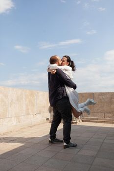 Happy married couple celebrating relationship anniversary on building rooftop enjoying romantic panoramic view. Caucasian wife and husband hugging at observation point with metropolitan city panorama