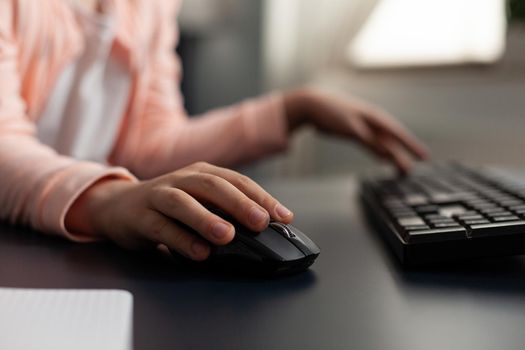 Close-up little schoolkid hands typing literature homework using computer keyboard sitting at desk studying online school lesson in living room. Concept of distance education at home