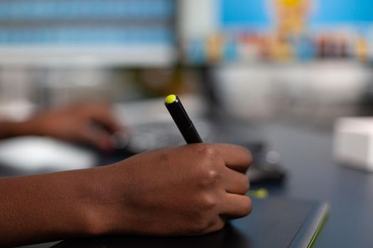 Close up of african photographer holding stylus pen editing creative photo using computer with two displays. Black woman editor retouching assets drawing on graphic tablet in creative agency office