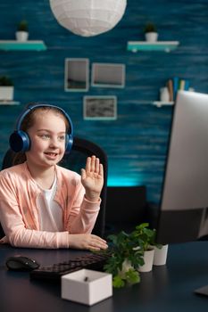 Smiling schoolkid wearing headset greeting remote teacher during online videocall meeting conference attenting to school lesson. Concept of distance education at home during coronavirus quarantine