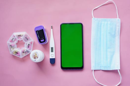 flat composition of smart phone, mask, thermometer and sanitizer on table .