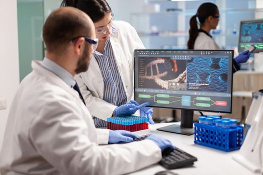 Group of scientists working in modern equipped laboratory pointing on computer desktop. y pointing on computer desktop. Chemists stuff analysing virus evolution using high tech technology for treatment research.