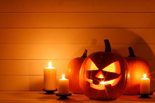 Halloween pumpkin glowing jack o lantern with carved face and candles on wooden background, banner with copy space for text