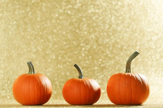 Three Pumpkins on golden glittery background with bokeh lights and copy space for text