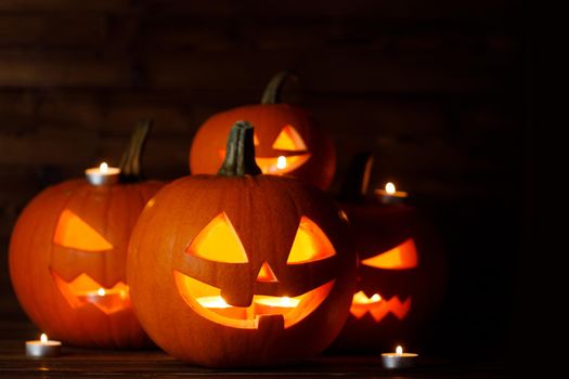 Group of glowing Halloween Pumpkin lanterns and burning candles on dark wooden background
