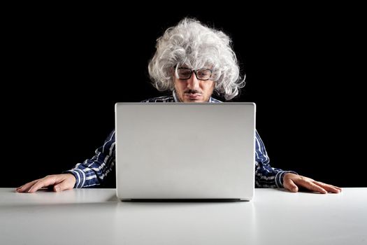 A boomer senior-focused concentrated sit at the desk looking at laptop computer on black background