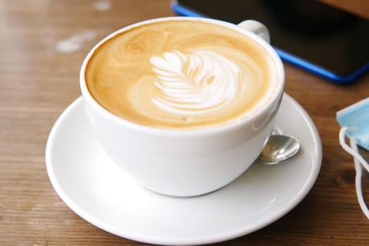 a cup of late coffee with flower shape design on top at cafe .