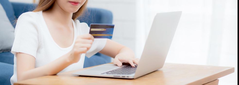 Young asian woman sit on sofa using laptop computer shopping online with credit card buying to internet, happy girl payment with e-business on couch, purchase and payment, business concept.