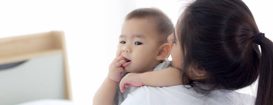 Young asian mother holding little baby girl together in the bedroom at home, mom carry child and care, woman and kid with carefree, toddler and parent, emotion and expression, family concept.