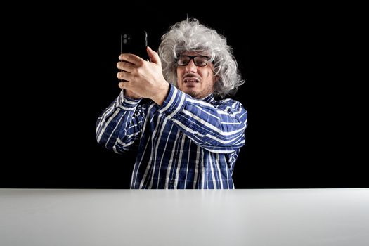 Smiling man sitting at the desk having a videochat talking on smartphone on black background