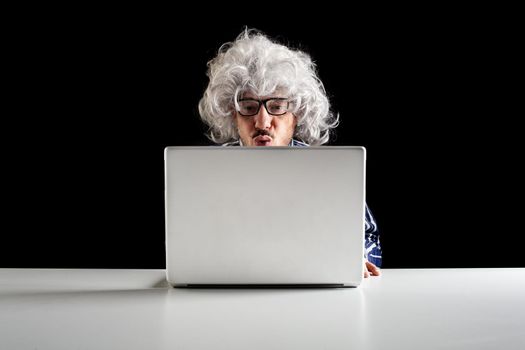 A boomer senior-focused concentrated sit at the desk looking at laptop computer on black background