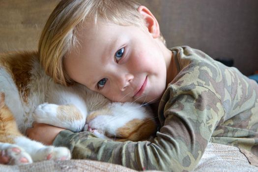 Portrait of happy adorablechild aged four years old on the bed in his room whit sleeping red cat. Thoughtful look. High quality photo
