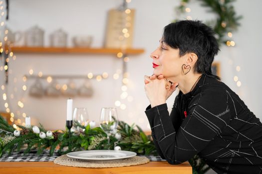 Portrait of stylish adult brunette woman making a Christmas wish at the table.