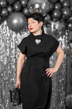 Stylish woman in elegant black dress posing on silver background.