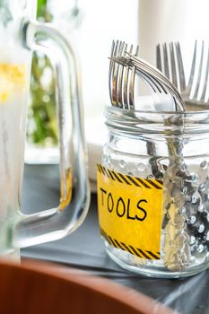 A close up photograph of forks in a textured glass mason jar on black table cloth with the word tools written on a yellow and black striped label for a kids birthday party with construction theme.