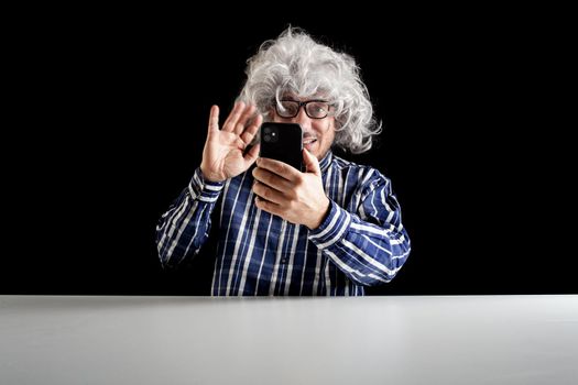 Smiling man sitting at the desk having a videochat talking on smartphone on black background