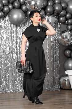 Stylish woman in elegant black dress posing on silver background.