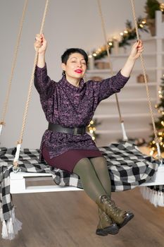 Smiling brunette woman with short hair, with tired eyes on a swing in the room.