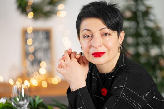 Portrait of stylish adult brunette woman making a Christmas wish at the table.