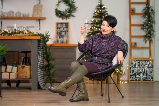 Short hair brunette woman with a glass of champagne sits on a chair celebrating christmas.