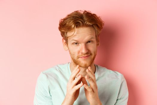 Close up of funny bearded man with red hair pitching a perfect plan, smiling and steeple fingers, scheming something, standing devious against pink background.