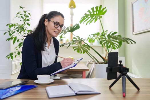 Middle aged business woman, teacher working from home remotely, using smartphone for video call, video conference. Freelance, distance business, technology, home Office, people concept