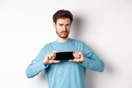 E-commerce and shopping concept. Sad and disappointed guy complaining, showing empty smartphone screen, standing on white background.