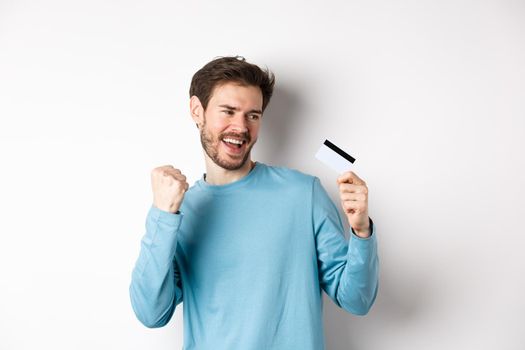 Happy man dancing with plastic credit card, smiling and saying yes, celebrating on white background. Copy space