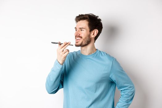 Young man talking on speakerphone or translating voice recording on application, standing happy on white background.