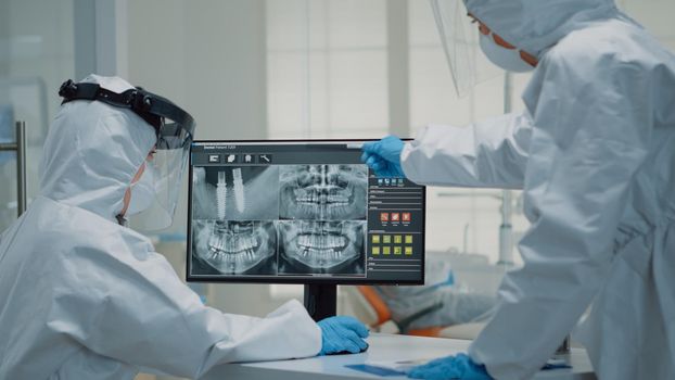 Team of stomatologists analyzing dental x ray scan on computer monitor at oral care clinic. Caucasian orthodontists examining teeth radiography with modern technology for implant