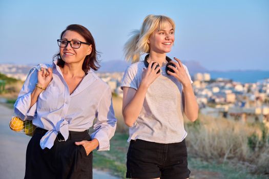 Beautiful talking mom and teenage daughter outdoors. Happy mother and teen girl walking together with eco shopper with oranges. Family, happiness, relationship parent teenager, summer, trendy, people