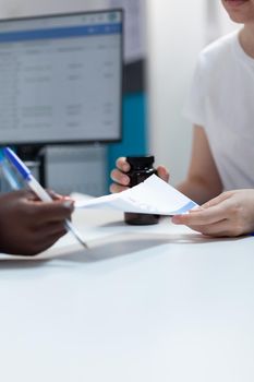 Closeup of african american therapist giving antibiotic prescription to patient during clinical consultation in hospital office. Woman holding pills bottle discussing disease symptoms with physician