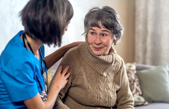 A young nurse takes care of an elderly 80-year-old woman at home, holds her hands . Happy retired woman and trust between doctor and patient. Medicine and healthcare.