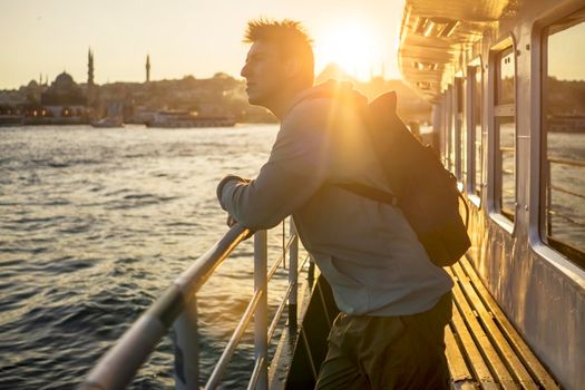 A young travelling man on a ferry floats to the shores of Istanbul, Turkey in the rays of sunset. The beginning of a great adventure.